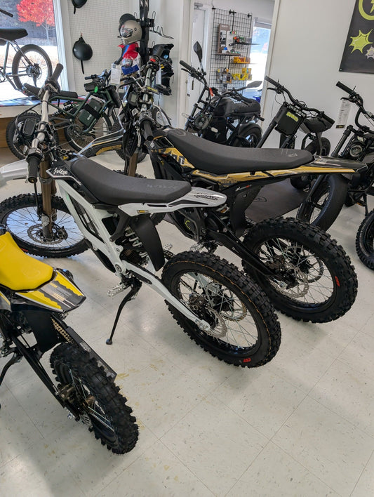 White Surron Light Bee 2 X beside black and gold Ultra Bee X HP at Radmoto